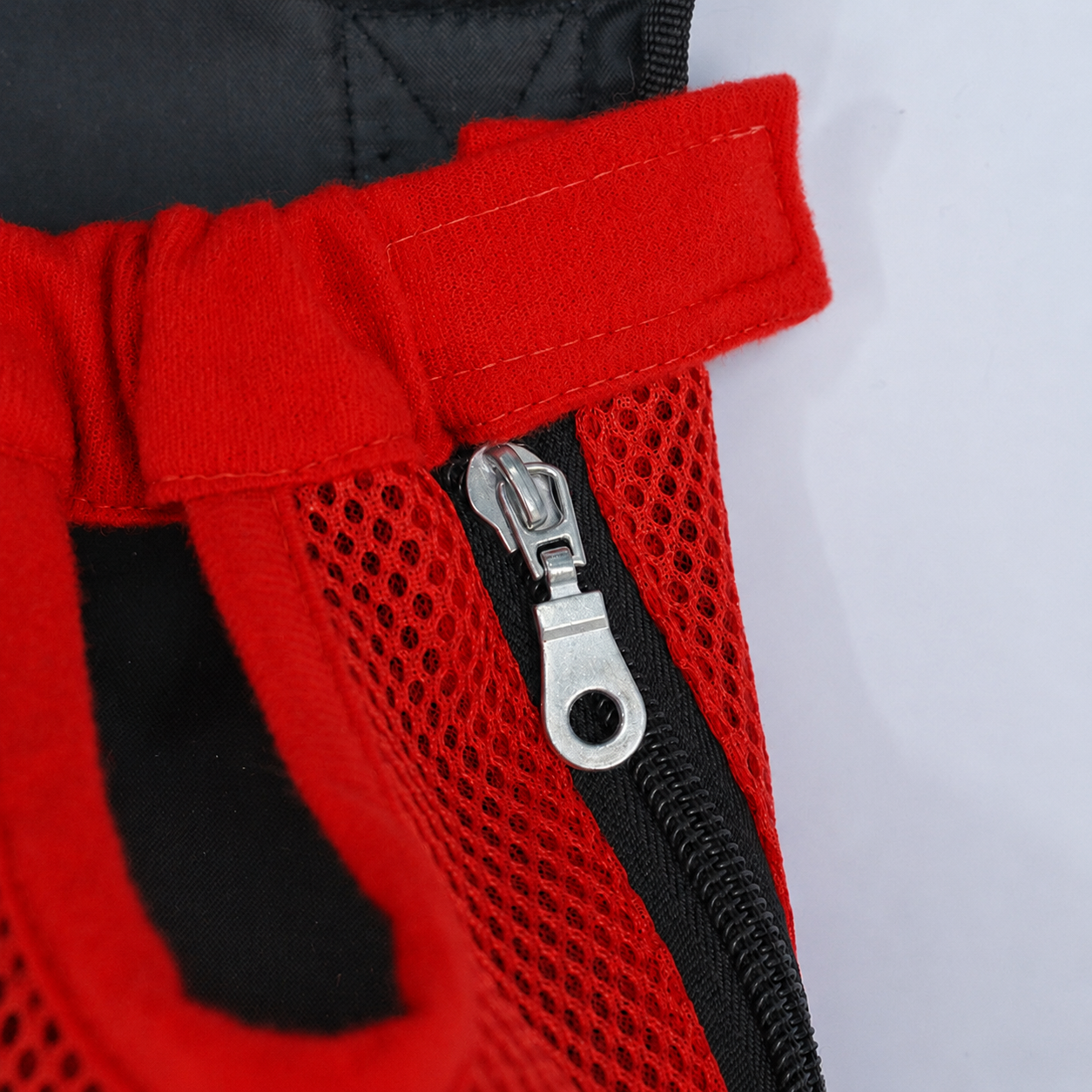 Gros plan sur la fermeture éclair latérale et la patte auto-agrippante du sac L'Éclaireur rouge, en maille respirante rouge