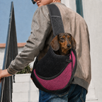 Petit teckel porté dans le sac de transport bandoulière Le Baladin rose, la tête sortie de la maille, un homme le porte en travers du buste dans la rue — Maison Pattounes